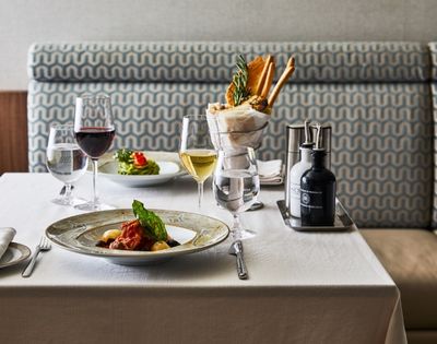 A restaurant table with elegant plating features a pasta dish, red and white wine, fresh salad, and breadsticks, set on a white tablecloth, creating a refined ambiance.