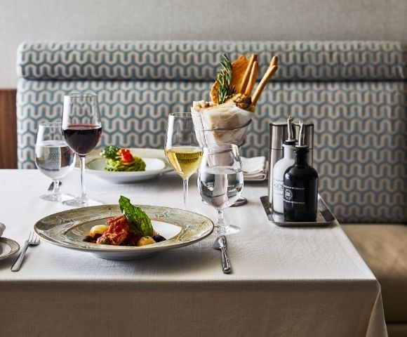 A restaurant table with elegant plating features a pasta dish, red and white wine, fresh salad, and breadsticks, set on a white tablecloth, creating a refined ambiance.
