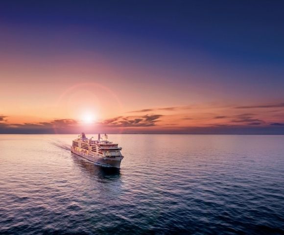 Cruise ship on calm ocean at sunset, with the sun low on the horizon, casting a warm glow across the sky and serene water, evoking relaxation and adventure.