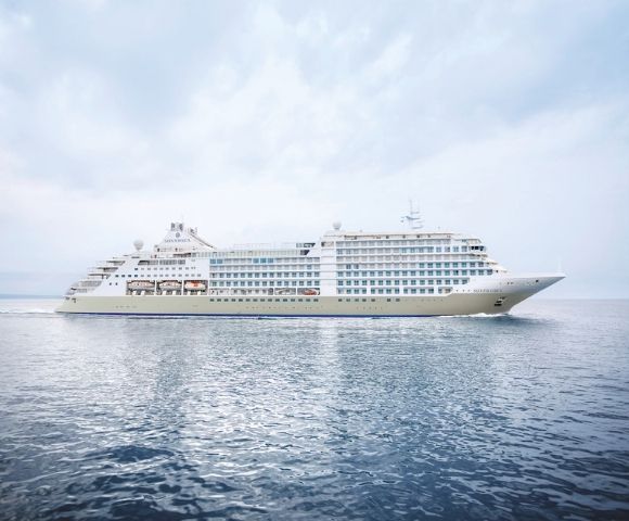 A large white cruise ship sails on calm blue waters under a cloudy sky. The serene scene conveys a sense of tranquility and luxury travel.