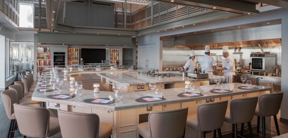 Luxurious open kitchen with marble countertops, plush chairs, and chefs in white uniforms preparing dishes, creating an elegant, professional ambiance.