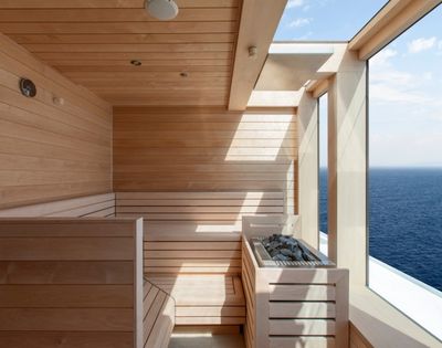 A modern wooden sauna with large windows overlooking the ocean. Sunlight filters in, creating a serene and relaxing atmosphere.
