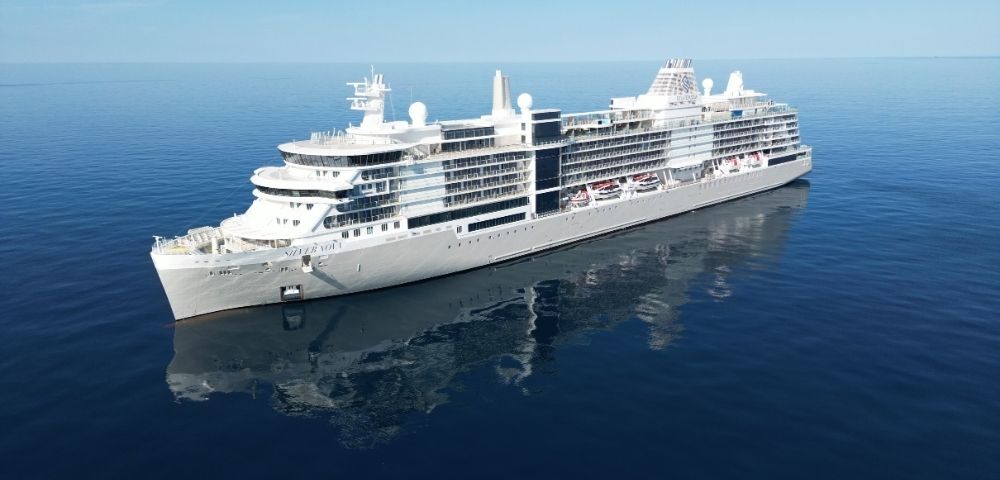A large white cruise ship sails smoothly on a calm, deep blue ocean under a clear sky, reflecting peacefulness and luxury travel.