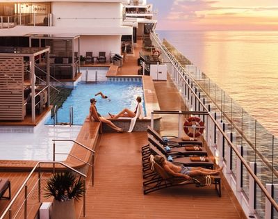 Sunset view from a cruise ship's deck with a pool. People relaxing on loungers, enjoying the serene sea and vibrant sky, creating a tranquil atmosphere.