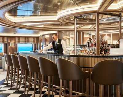 Luxurious cruise ship bar with elegant chairs and a polished counter. A bartender adjusts glassware, conveying a relaxed, upscale atmosphere.