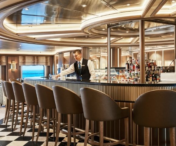Luxurious cruise ship bar with elegant chairs and a polished counter. A bartender adjusts glassware, conveying a relaxed, upscale atmosphere.