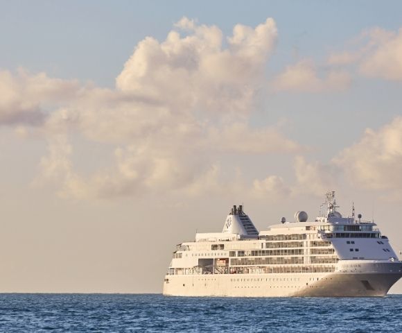 Cruise ship sailing on a calm ocean under a sky with fluffy clouds, evoking a serene and peaceful atmosphere.