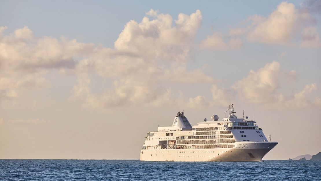 Cruise ship sailing on a calm ocean under a sky with fluffy clouds, evoking a serene and peaceful atmosphere.