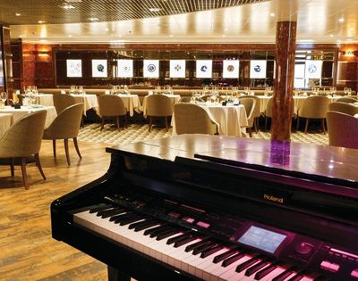 Grand piano in an elegant restaurant with round tables and beige chairs. Soft lighting and wall art create a sophisticated and inviting atmosphere.
