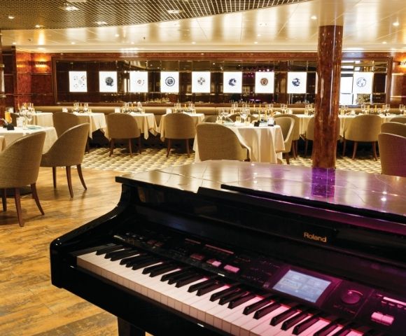 Grand piano in an elegant restaurant with round tables and beige chairs. Soft lighting and wall art create a sophisticated and inviting atmosphere.