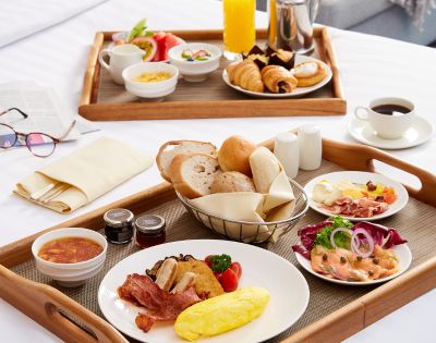 Elegant breakfast spread on wooden trays with croissants, bread, eggs, salmon, deli meats, and coffee on a white tablecloth, conveying a cozy, inviting morning.