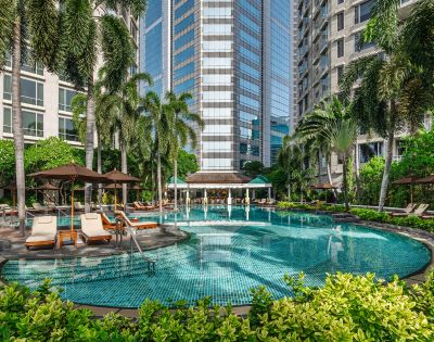 A tranquil hotel pool surrounded by lush palm trees and sun loungers, set against a backdrop of modern high-rise buildings. A relaxing oasis in the city.