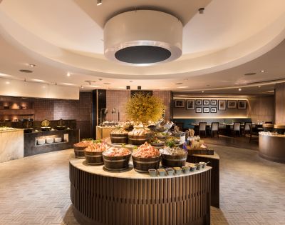 Luxurious buffet restaurant with elegant decor. Central circular table features seafood displays, surrounded by warm lighting and cozy seating.