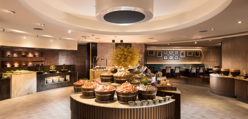 Luxurious buffet restaurant with elegant decor. Central circular table features seafood displays, surrounded by warm lighting and cozy seating.