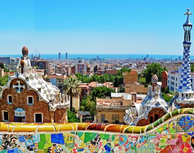 Colorful mosaic structures overlook a sprawling cityscape and distant ocean under a clear blue sky, capturing vibrant and artistic energy.