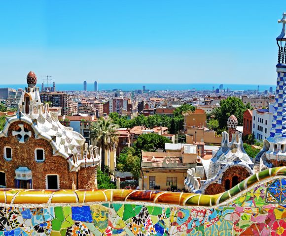 Colorful mosaic structures overlook a sprawling cityscape and distant ocean under a clear blue sky, capturing vibrant and artistic energy.