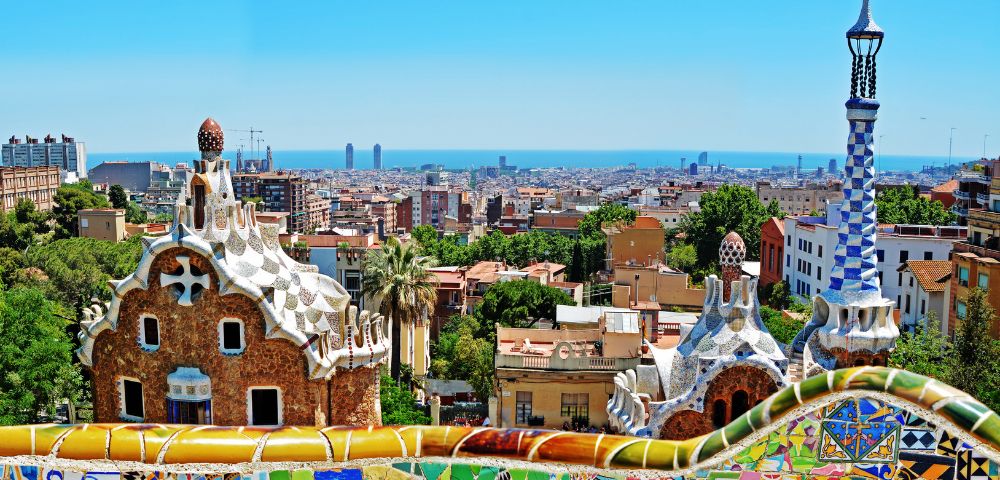 Colorful mosaic structures overlook a sprawling cityscape and distant ocean under a clear blue sky, capturing vibrant and artistic energy.