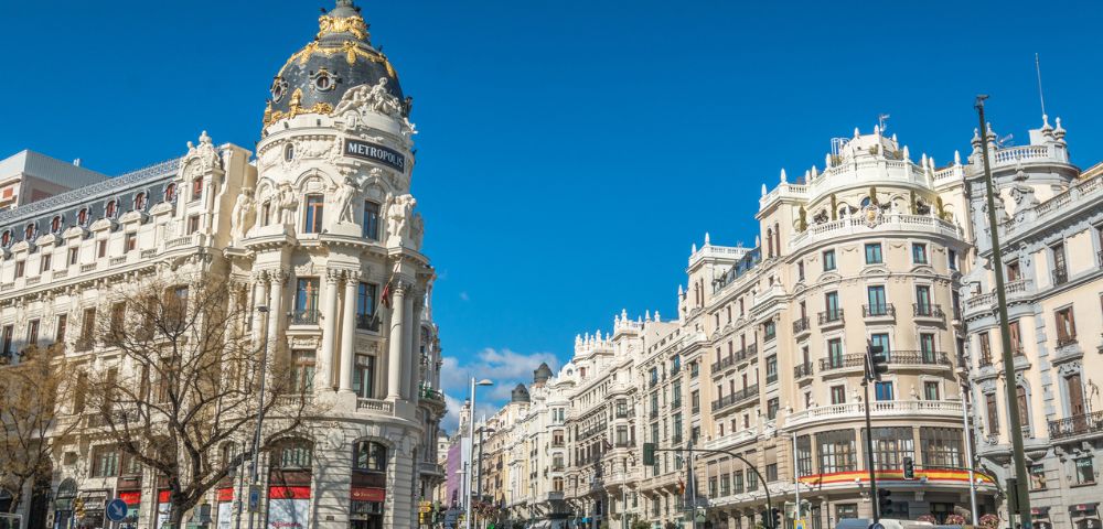 Bustling cityscape of Madrid on a clear day, featuring the ornate Metropolis Building with its iconic dome and nearby elegant, historic architecture.