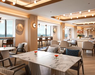 Stylish lounge with marble tables, modern chairs, and warm lighting. Large windows display a scenic view. Bright, inviting, and elegantly designed.