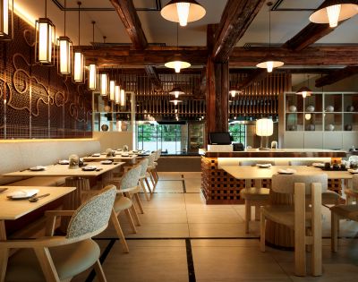 Elegant restaurant interior with wooden beams, warm lighting, and patterned walls. Tables are set for dining, creating a welcoming, cozy ambiance.