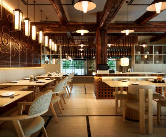 Elegant restaurant interior with wooden beams, warm lighting, and patterned walls. Tables are set for dining, creating a welcoming, cozy ambiance.