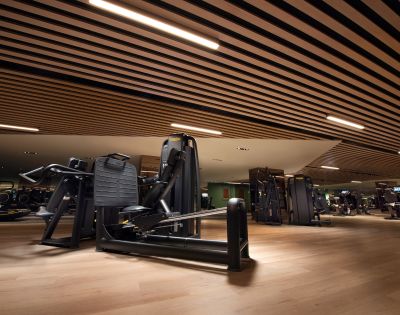 Modern gym interior with sleek black exercise machines on wooden floors. The ceiling features stylish wooden slats, creating a focused and energetic atmosphere.