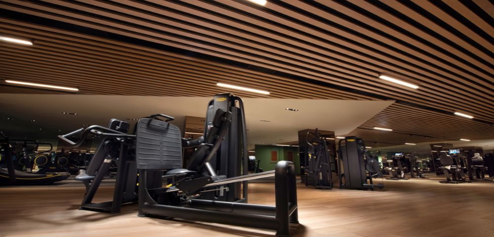 Modern gym interior with sleek black exercise machines on wooden floors. The ceiling features stylish wooden slats, creating a focused and energetic atmosphere.