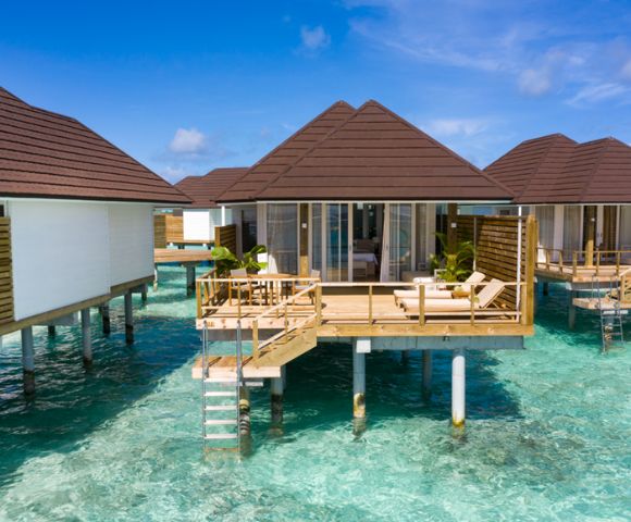 Overwater bungalows on stilts above turquoise ocean, under clear blue sky. Wooden decks with lounge chairs, creating a serene and tropical vacation vibe.