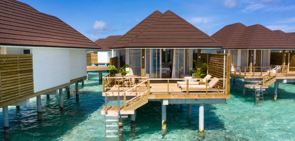Overwater bungalows on stilts above turquoise ocean, under clear blue sky. Wooden decks with lounge chairs, creating a serene and tropical vacation vibe.