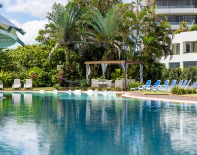 A serene pool at a beachfront resort, surrounded by palm trees and overlooking the ocean.