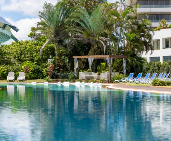 A serene pool at a beachfront resort, surrounded by palm trees and overlooking the ocean.