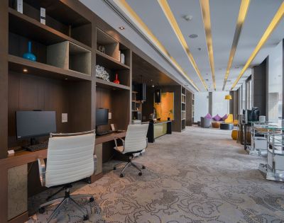 Modern office space with two white chairs and computers on wooden desks. Warm lighting, patterned carpet, and colorful bean bags create a relaxed atmosphere.