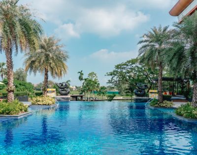 Luxurious pool surrounded by palm trees and tropical greenery under a bright blue sky. The serene and inviting scene conveys relaxation and leisure.