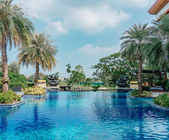 Luxurious pool surrounded by palm trees and tropical greenery under a bright blue sky. The serene and inviting scene conveys relaxation and leisure.