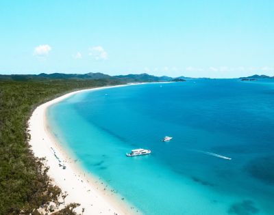 Aerial view of a serene beach with lush green hills, turquoise water, and two boats. The scene conveys tranquility and natural beauty.