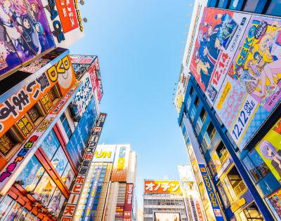 Urban skyline view in Akihabara, Tokyo, featuring colorful anime billboards on tall buildings under a clear blue sky, conveying a vibrant, energetic atmosphere.