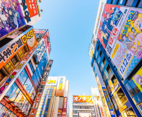 Urban skyline view in Akihabara, Tokyo, featuring colorful anime billboards on tall buildings under a clear blue sky, conveying a vibrant, energetic atmosphere.