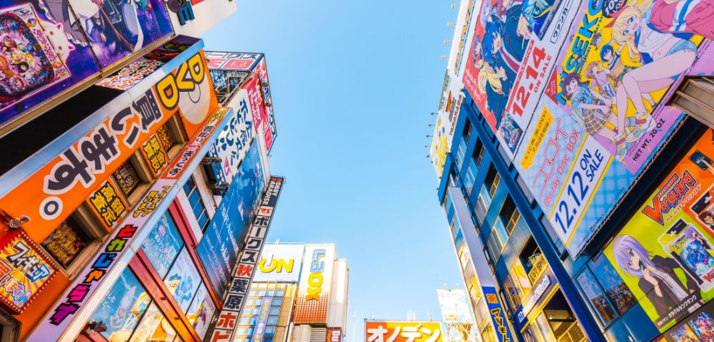 Urban skyline view in Akihabara, Tokyo, featuring colorful anime billboards on tall buildings under a clear blue sky, conveying a vibrant, energetic atmosphere.