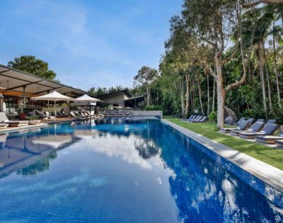 Luxurious poolside scene with clear blue water, surrounded by lounge chairs and lush trees. A serene atmosphere under a bright blue sky.