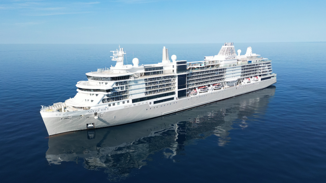 A large white cruise ship sails smoothly on a calm, deep blue ocean under a clear sky, reflecting peacefulness and luxury travel.