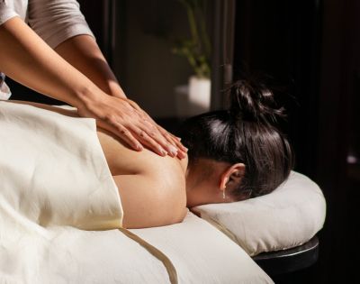 Woman receiving a relaxing back massage in dimly lit spa setting, conveying calm and serenity. A white towel covers her lower body.
