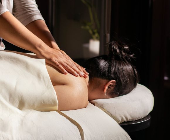 Woman receiving a relaxing back massage in dimly lit spa setting, conveying calm and serenity. A white towel covers her lower body.