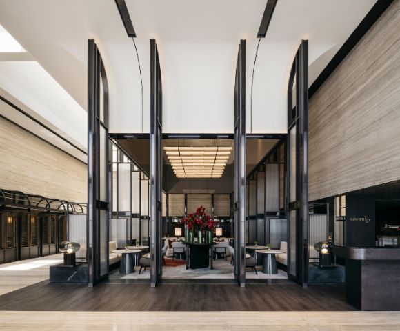 Spacious modern hotel lobby with high ceilings, sleek black partitions, and elegant seating. Red floral centerpiece adds a touch of vibrancy and luxury.