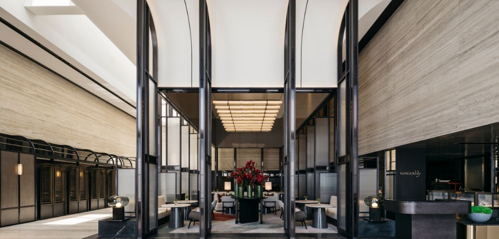 Spacious modern hotel lobby with high ceilings, sleek black partitions, and elegant seating. Red floral centerpiece adds a touch of vibrancy and luxury.