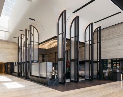 Modern hotel lobby with tall, arched glass panels and warm lighting. The space is open and minimalistic, creating a calm, elegant atmosphere.