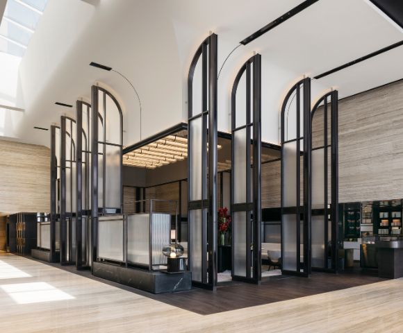Modern hotel lobby with tall, arched glass panels and warm lighting. The space is open and minimalistic, creating a calm, elegant atmosphere.