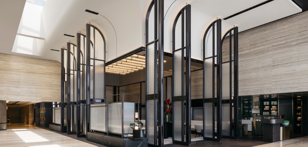 Modern hotel lobby with tall, arched glass panels and warm lighting. The space is open and minimalistic, creating a calm, elegant atmosphere.