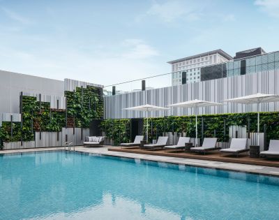 A serene outdoor pool with clear blue water surrounded by modern lounge chairs and umbrellas. Vertical garden walls enhance the minimalist, refreshing atmosphere.
