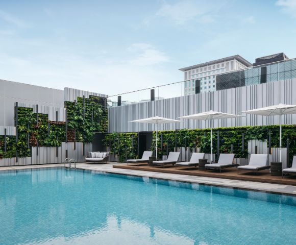 A serene outdoor pool with clear blue water surrounded by modern lounge chairs and umbrellas. Vertical garden walls enhance the minimalist, refreshing atmosphere.