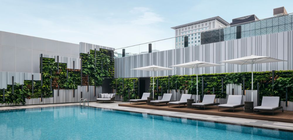 A serene outdoor pool with clear blue water surrounded by modern lounge chairs and umbrellas. Vertical garden walls enhance the minimalist, refreshing atmosphere.
